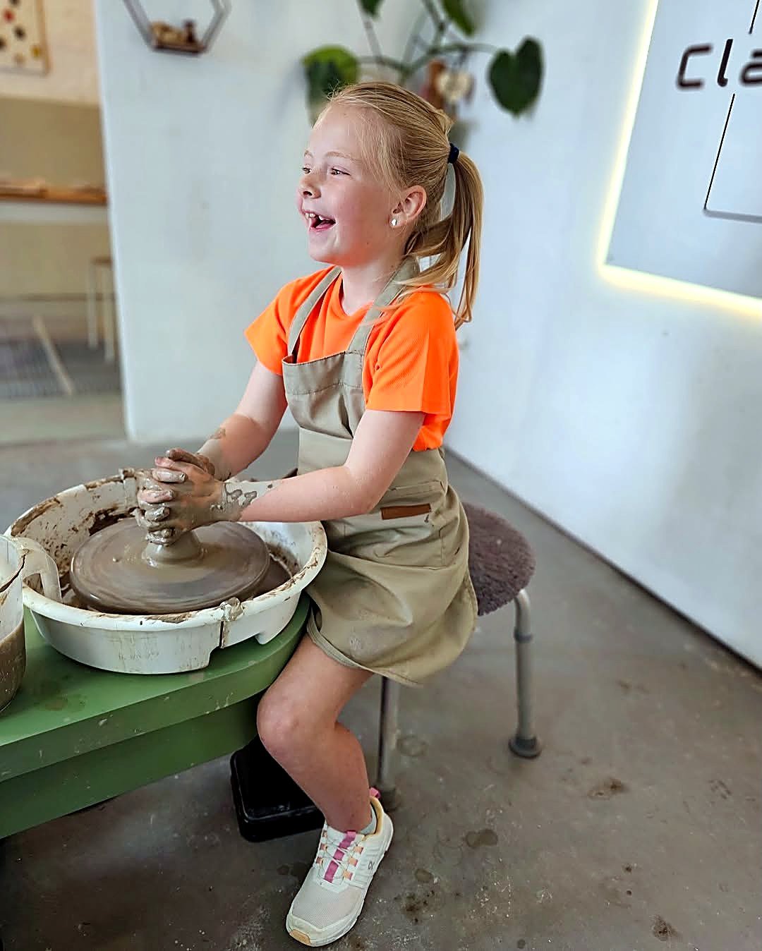 A young potter laughing while throwing on the wheel at Clay-Zy Day Studio